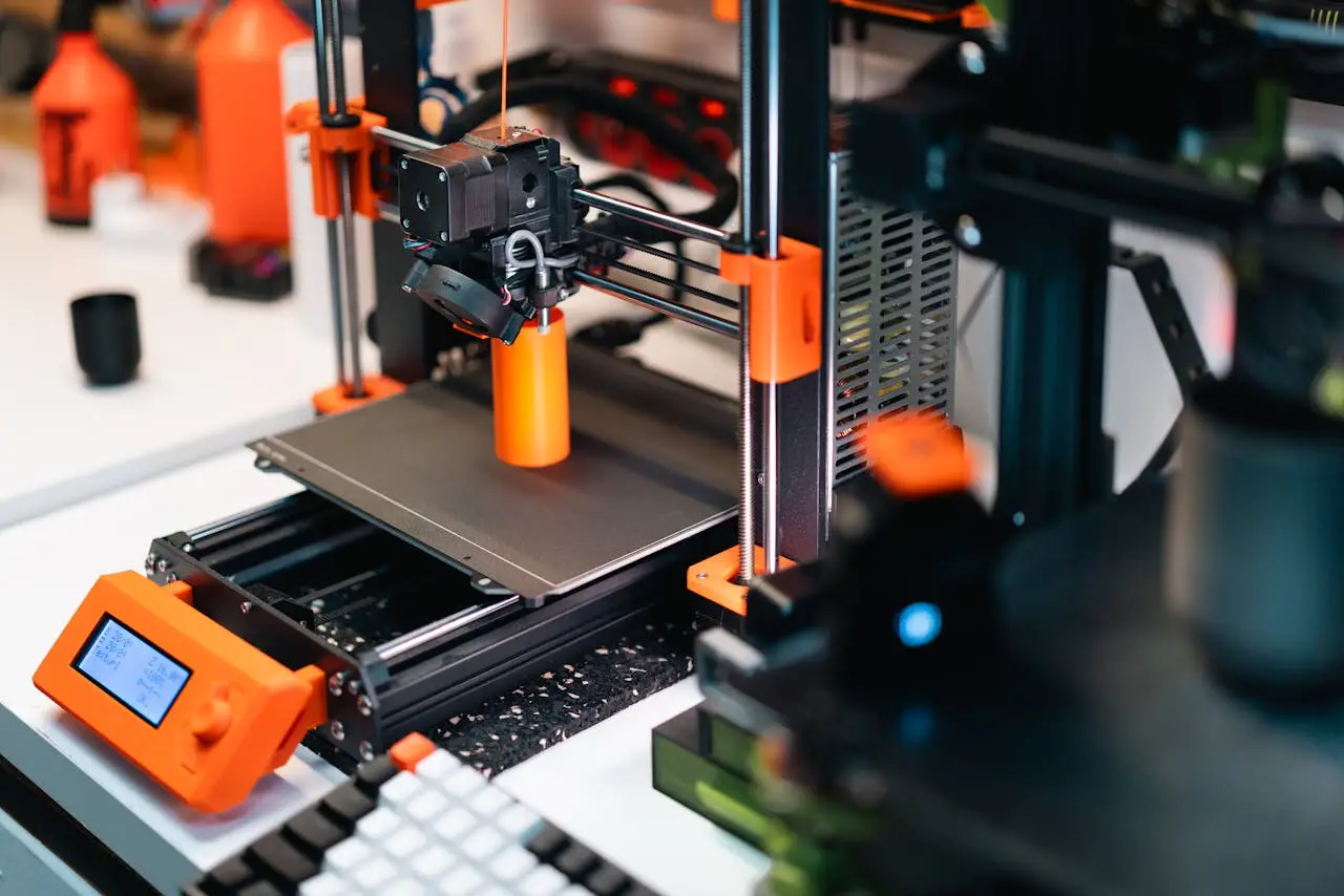 about-01 3D printer operating in a workshop, creating a prototype with orange accents.